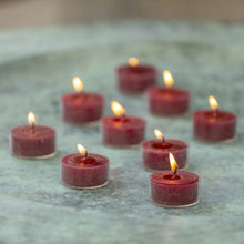Load image into Gallery viewer, Rustic coloured tealights in a bag of ten with glowing flames on a decorative surface.