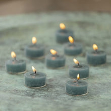 Load image into Gallery viewer, Rustic coloured tealights in petrol blue color with flames, arranged in a circular pattern on a decorative surface.