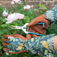 Charger l'image dans la galerie, gardening gauntlet gloves in RHS woodland wonders design being used to trim roses with gardening shears.