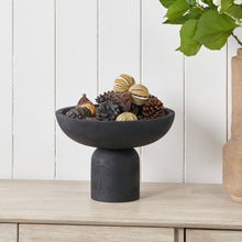 Lade das Bild in den Galerie-Viewer, Decorative black wooden pedestal bowl with natural elements on a wooden surface against a white paneled wall.
