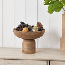Lade das Bild in den Galerie-Viewer, Wooden pedestal bowl with decorative items on a wooden surface against a white paneled wall.

