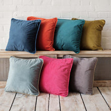 Indlæs billede til gallerivisning Collection of velvet velour cushions in various colors with coordinating piping on a wooden surface.
