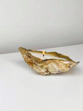 Load image into Gallery viewer, Shell candle in a recycled oyster shell with a gold tip and burning wick on a white surface.
