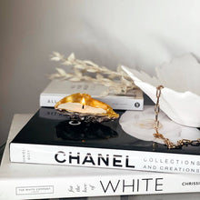 Load image into Gallery viewer, Shell candle in recycled oyster shell with gold tip, placed on a stack of books for an elegant home decor.

